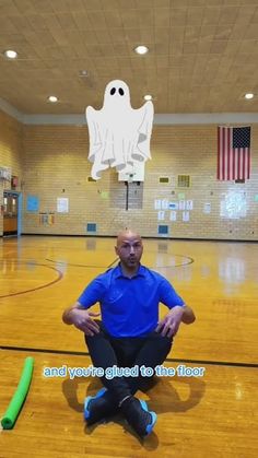 a man sitting on the floor in front of a basketball court with a ghost above him