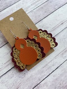 the earrings are made out of leather with gold and red details on them, sitting on top of a piece of cardboard