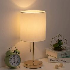 an alarm clock sitting on top of a table next to a lamp and some books