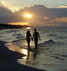 two people walking on the beach at sunset