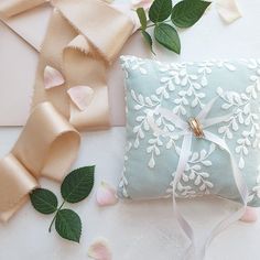 a blue and white pillow sitting on top of a table next to pink flowers with ribbons around it