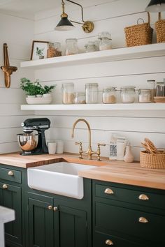 a kitchen with green cabinets and wooden counter tops, gold faucet, white shiping on the wall