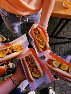 four hotdogs with toppings are sitting on paper trays at a table