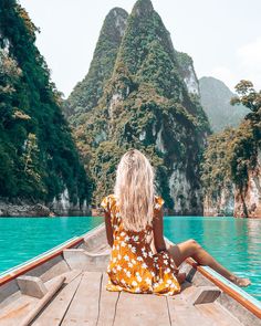 a woman sitting on the back of a boat looking out at mountains and blue water