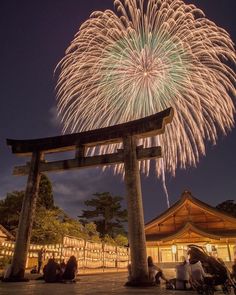 fireworks are lit up in the night sky above a gate and people sitting under it