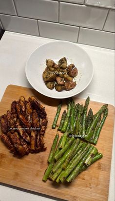 asparagus and other vegetables on a cutting board next to a bowl of potatoes