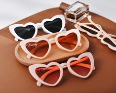 three pairs of heart shaped sunglasses sitting on top of a wooden tray next to a bottle