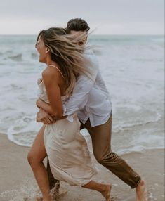 a man and woman are running on the beach in front of the ocean while holding each other