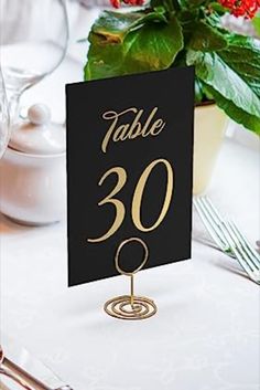 the table numbers are black and gold on this place card holder for guests to write their names