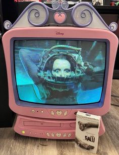 an old pink tv sitting on top of a wooden floor in front of a shelf