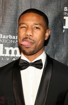 a close up of a person wearing a suit and bow tie with his tongue out