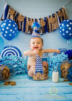 a baby is sitting in a cookie jar surrounded by cookies and blue decorations for his first birthday