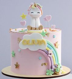 there is a pink cake with a unicorn on top and rainbow decorations around the edges