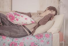 a woman laying on top of a bed next to pillows and pillow cases with pink flowers