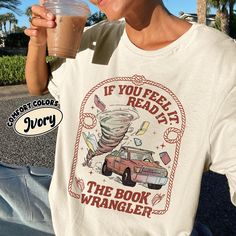 a young man holding a drink in his right hand while wearing a t - shirt that reads if you feel ready, the book wrangler