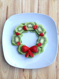 sliced kiwis and strawberries arranged in a wreath on a white plate with a wooden table