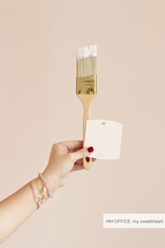 a hand holding a paint brush with a card attached to it