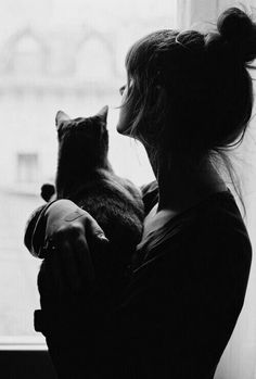 a black and white photo of a woman holding a cat in front of a window