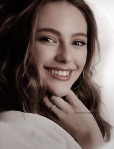 a woman smiling with her hand on her chin, wearing a white shirt and posing for the camera