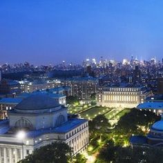 an aerial view of the city skyline at night with buildings lit up and trees in the foreground