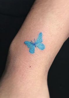 a small blue butterfly tattoo on the wrist