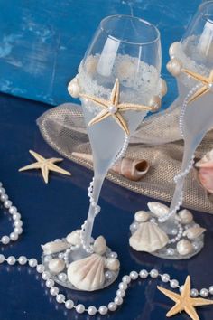 two champagne flutes with seashells and pearls on a blue table cloth next to shells