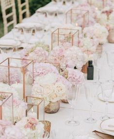 a long table with white and pink flowers in vases, candles and place settings