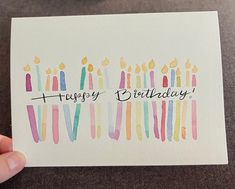 a hand holding up a card with candles on it and the words happy birthday written in black ink