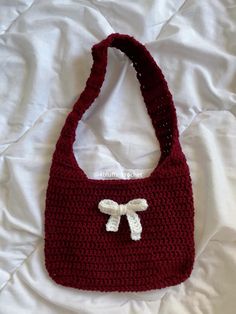 a crocheted purse with a white bow on the front and side, sitting on a bed