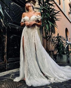 a woman standing in front of a building wearing a white dress with high slits