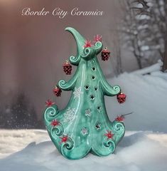 a green ceramic christmas tree with red berries and pine cones on it in the snow