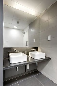 two white sinks sitting on top of a black counter next to a wall mounted mirror