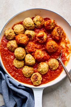 a pan filled with meatballs and sauce on top of a blue towel next to a fork