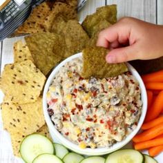 a bowl of dip surrounded by carrots, cucumbers and crackers