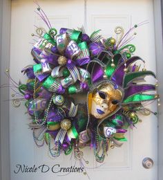 a mardi gras wreath with purple and green decorations hanging on a white door