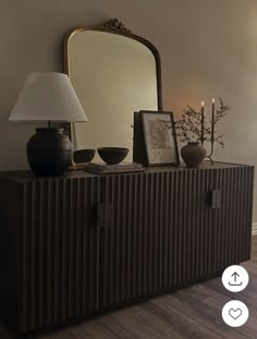 a dresser with a mirror and vases on top of it next to a lamp