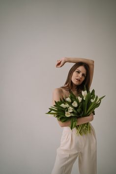 a woman holding flowers in her hands and posing for the camera with one hand on her head