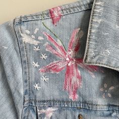 a pink flower painted on the back of a jean jacket