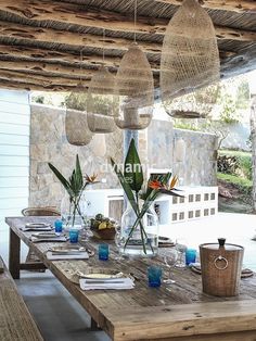 a wooden table with plates and glasses on it under an outdoor covered area that has stone walls