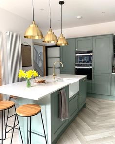 a kitchen with green cabinets and gold pendant lights