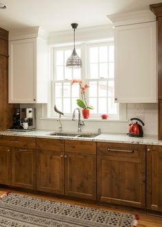 a kitchen with wooden cabinets and white counter tops, an area rug on the floor