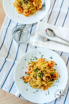 two plates of pasta with shrimp and parsley on the side next to silverware