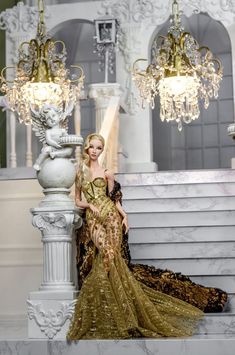 a woman in a gold dress standing next to a chandelier and marble steps