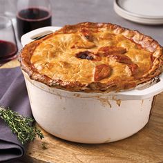 a pot pie sitting on top of a wooden cutting board next to a glass of wine