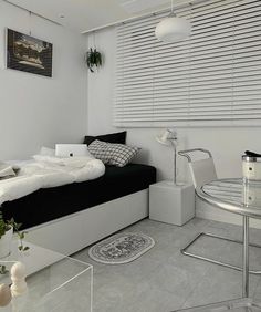 a bedroom with white walls and flooring, black and white bedding, glass table and chairs