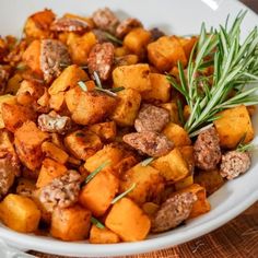 a white bowl filled with meat and vegetables on top of a wooden table next to utensils