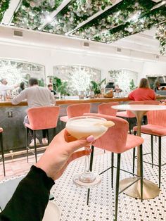 a person holding up a wine glass in front of a bar with people sitting at tables