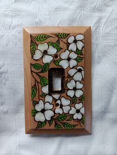 a wooden light switch cover with flowers painted on the front and back sides, sitting on a white sheet