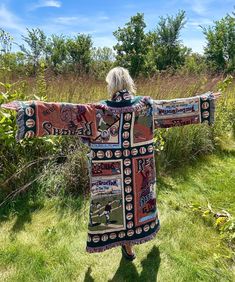 a woman standing in the grass with her arms spread out and wearing a colorful coat