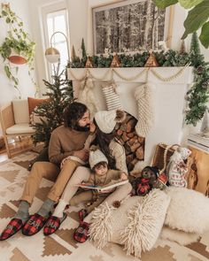 a man and woman are sitting on the floor with their children in front of a christmas tree